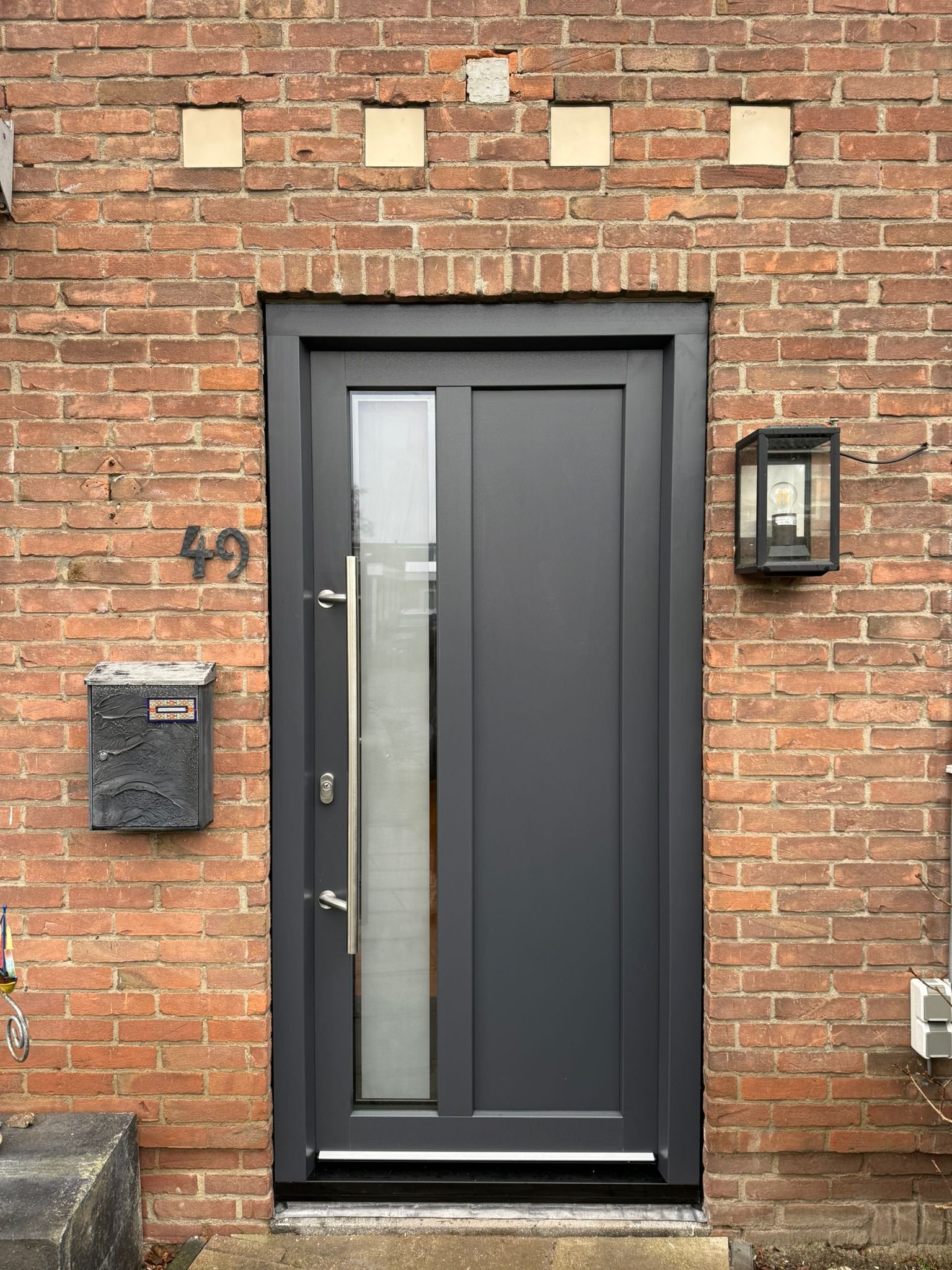 Antraciet kunststof voordeur met verticaal glaspaneel en rvs greep